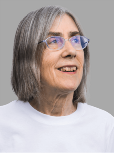 Helene Bouchiat mit weißem Pulli, Brille und grauem Haar, lächelnd vor grauem Hintergrund.